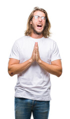 Young handsome man with long hair wearing glasses over isolated background begging and praying with hands together with hope expression on face very emotional and worried. Asking for forgiveness.