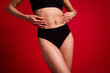 © deagreez - Cropped photo of pretty young girl touch belly waist skin wear black underwear no retouch isolated on red color background