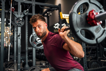 A strong young adult man lifting weight and squatting at the gym