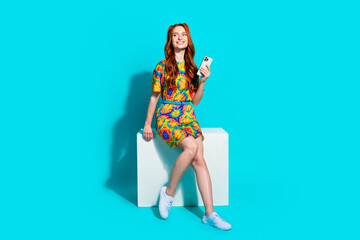 Canvas Print - Full size photo of pretty young girl sit cube hold device look empty space wear colorful outfit isolated on aquamarine color background