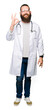© Krakenimages.com - Young blond doctor man with beard wearing medical coat smiling positive doing ok sign with hand and fingers. Successful expression.