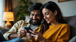 © mischenko - indian couple smiling and looking at phone sitting on sofa at home