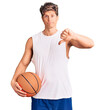 © Krakenimages.com - Young handsome man holding basketball ball with angry face, negative sign showing dislike with thumbs down, rejection concept