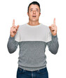 © Krakenimages.com - Handsome young man wearing casual winter sweater amazed and surprised looking up and pointing with fingers and raised arms.