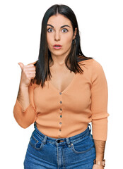 Wall Mural - Young hispanic woman wearing casual clothes surprised pointing with hand finger to the side, open mouth amazed expression.