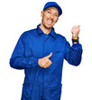 © Krakenimages.com - Bald man with beard wearing builder jumpsuit uniform pointing to the back behind with hand and thumbs up, smiling confident