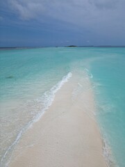 The photo shows an aerial view of Dhigurah Island in the Maldives, featuring a long stretch of lush greenery bordered by pristine white sand beaches and crystal-clear turquoise waters. 