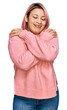 © Krakenimages.com - Hispanic woman with pink hair wearing casual winter sweater hugging oneself happy and positive, smiling confident. self love and self care