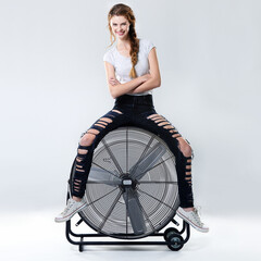 Portrait, smile and woman on electric fan for fashion in studio on white background. Happy girl, relax and air blower for cool style, creative clothes and edgy with arms crossed for confidence in USA