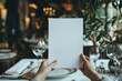 © whoopwhoops - hand holdin a blank Menu paper, luxury restaurant table with a plate and silver cutlery background, blank mock up menu sheet