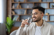 © Tetiana - Young Hispanic man enjoying refreshing glass of water at home with relaxed expression and casual attire