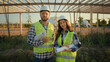 © Yuliia - Happy successful engineers Caucasian workers smiling woman female girl professional man male guy in uniform hardhat helmet looking at camera holding blueprint plan project outside park farmland nature