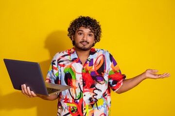 Wall Mural - Photo portrait of attractive young man hold netbook shrug shoulders dressed stylish colorful clothes isolated on yellow color background