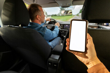 Taxi service application. Female passenger holding smartphone with blank screen while driver man driving car, woman sitting on backseat in auto. Mockup