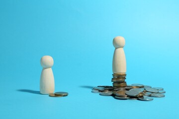 Wall Mural - Financial inequality. One wooden figure on bigger stack of coins than another on light blue background