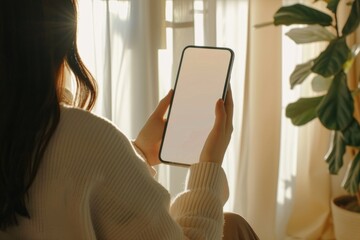 Canvas Print - A woman is holding her phone in front of a window, possibly checking messages or taking a selfie