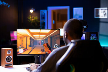 Wall Mural - Man in living room playing video games on gaming PC at computer desk, enjoying day off from work. Gamer battling enemies in online multiplayer shooter from neon lights ornate home