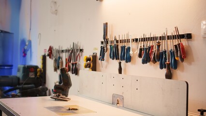 Wall Mural - Close up of electric router on spindle moulder in furniture assembly shop with woodworking tools on rack in background. Focus on hand powered equipment used for sanding wood in studio, panning shot