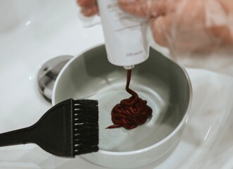 woman pours hair red dye in a bowl for dyeing red color using a special brush