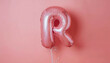 © Anna - Metallic pink balloon shaped like the letter 'R' tied with a white string. The balloon is centered against a solid pink background, creating a simple, minimal composition.