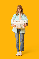 Young woman with laundry basket on yellow background