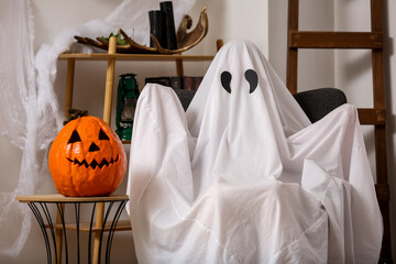 Sticker - Person in Halloween costume of ghost with carved pumpkin sitting on armchair at home