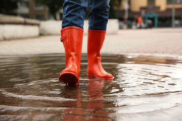 Wall Mural - Woman wearing orange rubber boots standing in puddle outdoors, closeup