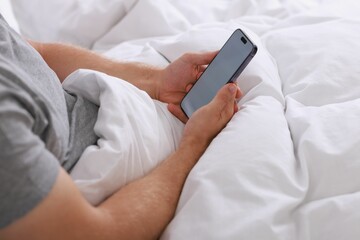 Man using smartphone in bed, closeup view