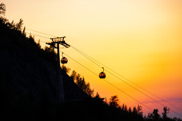 Silhouette of a cable car cabin against the backdrop of a sunset in the mountains.