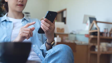 Canvas Print - Young woman typing text message on smart phone in a cafe. Asian woman in casual wear sitting at a table with a coffee using mobile phone in coffee shop.