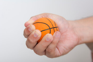 Closeup shot of a male hand squeezing a stress ball that resembles a miniature basketball. A novelty item or toy.