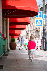 Wall Mural - A little girl walks along a city street with red canopies of a building in the center of St. Petersburg.