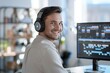 © miss irine - Man sits at desk wearing headphones smiling at camera. Works on computer with video editing software. Minimalistic workspace features bright studio. Editor focused on project with tidy classic shirt.
