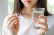 © Vadym - Close-up of young Asian woman holding pill capsule for stomach pain treatment. She takes a glass of water with vitamin or medicine for headache relief.