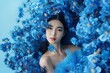 © miss irine - Asian woman poses elegantly in blue dress with flower arrangement. High-end fashion concept features perfume inspiration. Woman face hidden by flowers, dressed in blue attire on blue background.