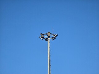 A tall metal streetlight with multiple lamps set against a clear blue sky. The minimalist composition highlights the modern urban infrastructure and clean background.