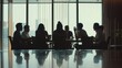 © VK Studio - A group of people in a meeting room, silhouettes against large windows, deep in discussion, capturing a dynamic business atmosphere.