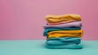 © VK Studio - A pastel stack of folded clothes against a pink background, showcasing a range of soft fabrics and hues for a soothing look.