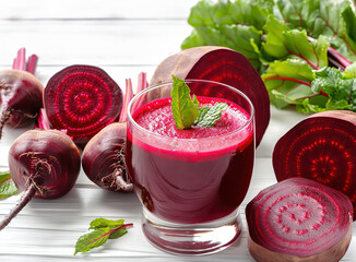 Glass fresh beet juice in center, decorated with mint surrounded by whole red beet cut into pieces