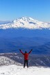 © stopcontrol - A hiker standing on a snow-capped mountain, with arms raised in celebration of reaching the summit
