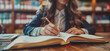 © Destri - Close up of a woman's hand writing in a book, sitting at a table in a library. Concept of learning, reading, education, and research.