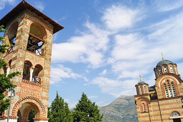 Architecture of the Hercegovacka Gracanica Monastery: a bell tower and a Byzantine-style church against a blue sky with clouds. View of the famous landmark of Trebinje (Bosnia and Herzegovina) 