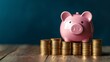 © marwan - Piggy bank sitting on a stack of coins, on a wooden table with blue background.