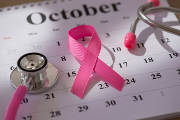 Pink ribbon and stethoscope placed on an October calendar to symbolize breast cancer awareness and health prevention concepts