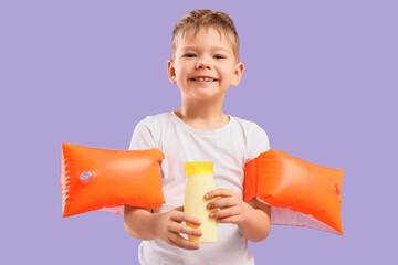 Wall Mural - Cute little boy with sunscreen cream and swim armbands on lilac background