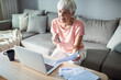 © Marko Geber - Senior woman managing finances on laptop at home