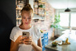 © Geber86 - Smiling young woman using smartphone in modern kitchen
