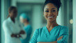 © Michael - Smiling young female medical professional with arms crossed, surrounded by colleagues in the background