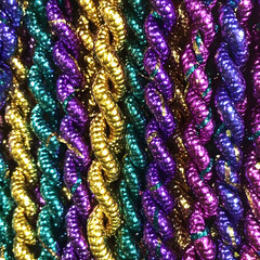 A close-up image of traditional Mardi Gras beads in vibrant gold, green, and purple colors showcasing their shiny textures and intricate designs