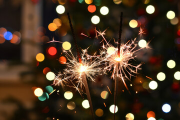 Two sparklers burning with christmas tree lights in background